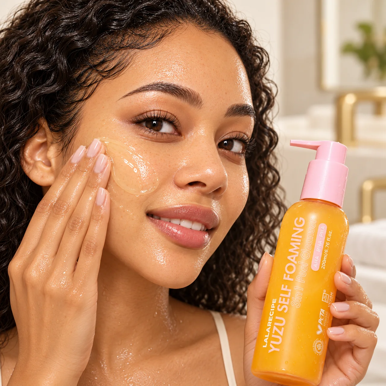 Woman working clear gel cleanser onto her cheek while holding the Yuzu cleanser bottle